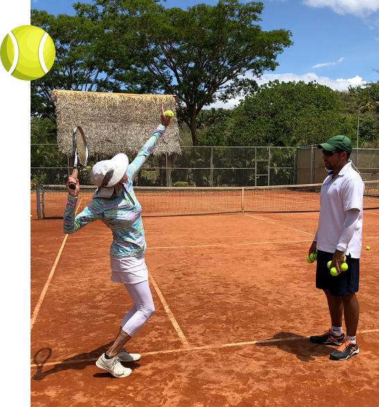 A student at an OTI in-person clinic practicing a serve with a coach on a hard court